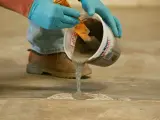 Man con guantes azules vierte hormigón líquido de un cubo para reparar el suelo. Aprende como hacer hormigón para suelo.