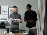 Two men review documents and a tablet, discussing the details of in-kind donation accounting.
