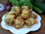 Frittelle di zucchine dorate e croccanti, pronte per essere gustate. Sullo sfondo, cipolle rosse, basilico fresco e zucchine.