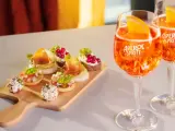 Zwei Aperol Spritz Gläser mit Orangenscheiben und eine Holzplatte mit verschiedenen Häppchen. Perfekt für einen Aperitif!
