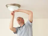 Mężczyzna wymienia żarówkę w lampie sufitowej, wykonując retrofit LED.