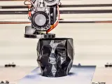 A 3D printer nozzle extrudes filament to create a faceted black skull planter, showcasing innovative 3D printing examples.