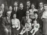 Gros plan sur une famille nombreuse posant pour une photo. On peut y voir des enfants, des adultes et des bébés. Une recherche sur Geneanet pourrait révéler leur nom de famille.