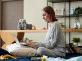 Kobieta na łóżku pisze wniosek o urlop rodzicielski na laptopie, otoczona zabawkami i pluszakami.