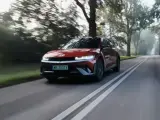 Czerwony Hyundai Ioniq 5 jedzie po wiejskiej drodze wśród drzew.