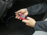 Ręce trzymające czerwony interfejs diagnostyczny OBDII/EOBD, podłączony do samochodu.