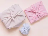 Trois paquets cadeaux joliment emballés dans des tissus de différentes couleurs (beige, rose, bleu clair). Lequel tissu pour furoshiki ? Le lin semble idéal.