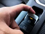 Dłoń naciska przycisk elektrycznego hamulca postojowego. Pomoc w zrozumieniu, jak wyłączyć elektryczny hamulec postojowy.