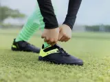 Dłonie wiążą sznurówki czarnych butów sportowych z neonowożółtymi wstawkami na zielonej murawie. To pierwszy krok, by dowiedzieć się, jak rozciągnąć buty sportowe.