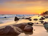 Zachód słońca nad Bałtykiem na Pomorzu Zachodnim. Fale obmywają kamienistą plażę, a niebo mieni się odcieniami pomarańczy i różu.