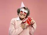 Uśmiechnięta starsza pani w okularach z napisem "Happy Birthday" i w czapce urodzinowej trzyma prezent. To dowcipne podziękowania za życzenia!