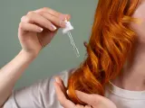Dłoń z pipetką z olejkiem aplikuje pielęgnację na rude, falowane włosy. Dowiedz się, jak często olejować włosy dla najlepszych efektów.