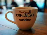 Taza de café blanca con la fórmula química de la cafeína y el texto "cafeína" impresos.