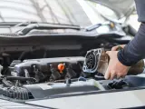 Mechanik wymienia rozrusznik w aucie. Widoczny jest silnik i ręce trzymające zużyty element.