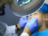 Dentysta w rękawiczkach bada usta dziecka pod lampą powiększającą.