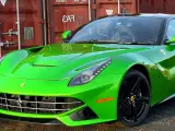 Jaskrawozielone Ferrari F12 Berlinetta z czarnymi felgami, zaparkowane przed czerwonym kontenerem.