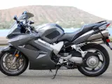 Szary motocykl Honda VFR 800 z widokiem na wodę i wzgórza w tle.