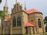 Gotycka ceglana świątynia z czerwonym dachem, jedna z krynki atrakcje. Wokół drzewa i trawnik.