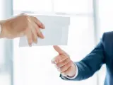 Main d'un homme en costume remettant une enveloppe blanche à une autre main. Peut-être une mise en demeure URSSAF avec un délai de paiement.