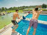 Zwei Jungen springen vom Sprungbrett in den Badesee Bremen. Im Hintergrund sind Wasserrutschen und viele Badegäste zu sehen.