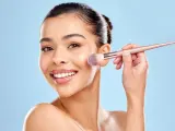 Une femme souriante utilise un pinceau pour appliquer du correcteur maquillage sur sa joue.