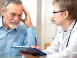 Arzt im Gespräch mit älterem Mann, der sich an die Stirn fasst.