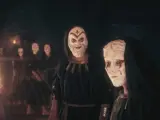 Miembros del culto de Kosmos, con túnicas oscuras y máscaras blancas, se reúnen ante un objeto piramidal brillante.