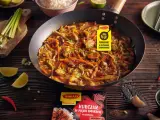 Kurczak w pięciu smakach po chińsku w woku, z warzywami i ryżem w tle. Obok limonki, chili i czosnek.