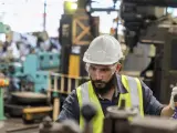 Obrero con casco y gafas de seguridad trabajando en una máquina en una fábrica, parte esencial de la manufactura moderna.