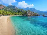Piękna plaża w Turcji, Kusadasi, z turkusową wodą, górami i sosnami. Idealne miejsce na wakacje.