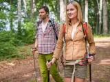 Ein Paar wandert achtsam durch einen Wald. Die Frau und der Mann nutzen Wanderstöcke, eine Anleitung für einen achtsamkeitsspaziergang.
