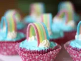 Sju cupcakes med ljusblå regnbågs frosting och godisregnbågar. Rosa muffinsformar med mönster.
