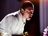 Mike Patton heute, mit weit aufgerissenem Mund und intensivem Blick, trägt ein weißes Hemd. Blumen im Vordergrund.