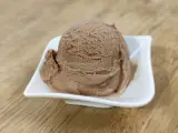 Ein Löffel cremiges Nougat Eis in einer weißen Schale auf einem Holztisch.