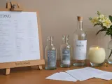 Na weselu kluczowe są zasady serwowania alkoholu, np. ile butelek na osobę. Na stole butelki, świeca i bukiet kwiatów.