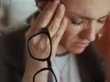 Kobieta z dłońmi na skroniach, trzymająca okulary, z wyrazem zmartwienia na twarzy.