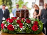 Czerwone róże i gipsówka otaczają urnę. Takie kwiaty na pogrzebie starszej osoby symbolizują miłość i pamięć.