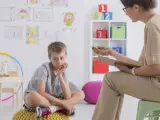 Chłopiec siedzi na poduszce, zastanawiając się, jakie pytania zadaje psycholog dziecku. W tle rysunki dzieci i kolorowe zabawki.