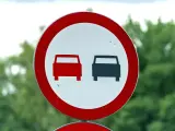 Znak drogowy: zakaz wyprzedzania. Dwa samochody, jeden czerwony, drugi czarny, stoją obok siebie.