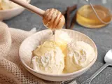 Schneeballgroße Kugeln Vanilleeis werden mit flüssigem Honig beträufelt. Ein Holzlöffel tropft goldenen Honig auf das cremige Eis.