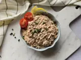 Un bol de rillettes de thon, garni de tomates cerises et de quartiers de citron, prêt à être dégusté.