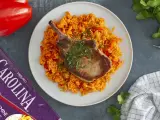 Chuleta de cerdo jugosa sobre arroz rojo con pimientos.