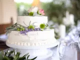 Dwupoziomowy tort weselny ozdobiony kwiatami, ziołami i oliwkami. Delikatne kremowe wykończenie i naturalne dekoracje podkreślają wyjątkowe smaki tortów weselnych.