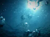 Bąbelki powietrza unoszą się w głębinach, gdzie światło słoneczne przebija się przez wodę, oświetlając grunty pod wodami powierzchniowymi płynącymi.