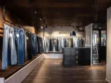 Jeans in vari lavaggi e tagli, inclusi modelli slim fit, esposti in un negozio moderno con pavimenti in legno scuro e illuminazione a faretti.