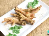 Patas de pollo sazonadas y listas para cocinar, adornadas con cilantro fresco sobre un plato blanco.