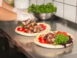 Ręce w rękawiczkach układają mięso na plackach z pomidorami i zieloną sałatą. Pyszny kebab gemuse gotowy do podania.