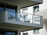 Nowoczesna loggia z przeszkloną balustradą, na której stoi stolik z kwiatami i krzesło.