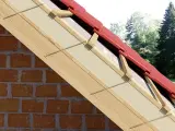 Ocieplenie nakrokwiowe dachu z czerwonej dachówki, widok przekroju z widoczną cegłą i drewnianą konstrukcją.