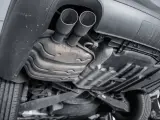 The underside of a car shows a dual exhaust system leading to a large muffler, which is a key component for reducing engine noise.